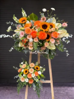 Rực rỡ Kệ Hoa Tươi Garden Nova phối cúc mẫu đơn cam và hướng dương nổi bật, chúc mừng khai trương sinh nhật. Vườn Hoa Tươi giao tận nơi HCM, đặt ngay!